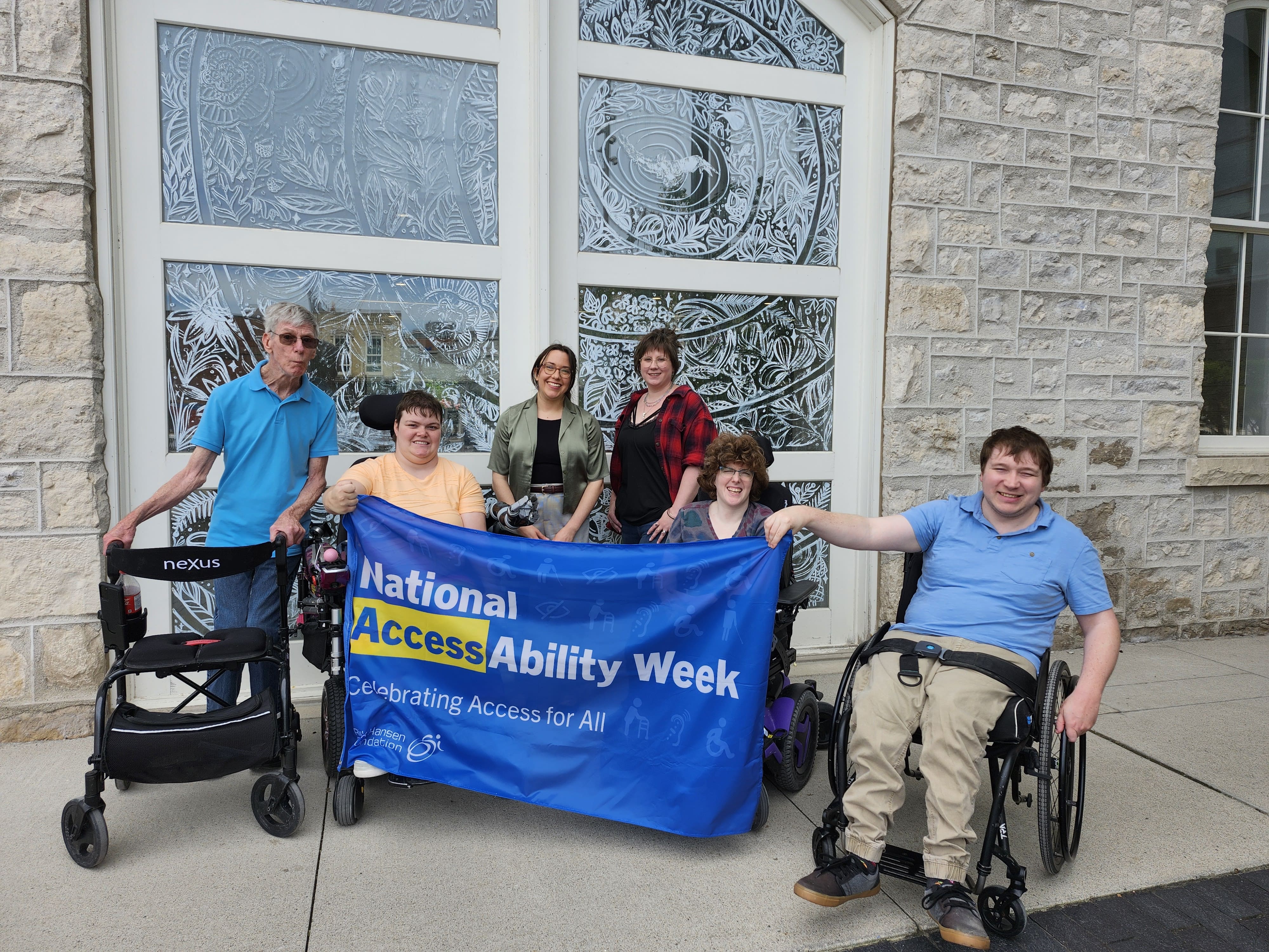 Brad, Maddy, Kayla, Meg, Kelsey and Justin gather together to hold the National AccessAbility Week flag.