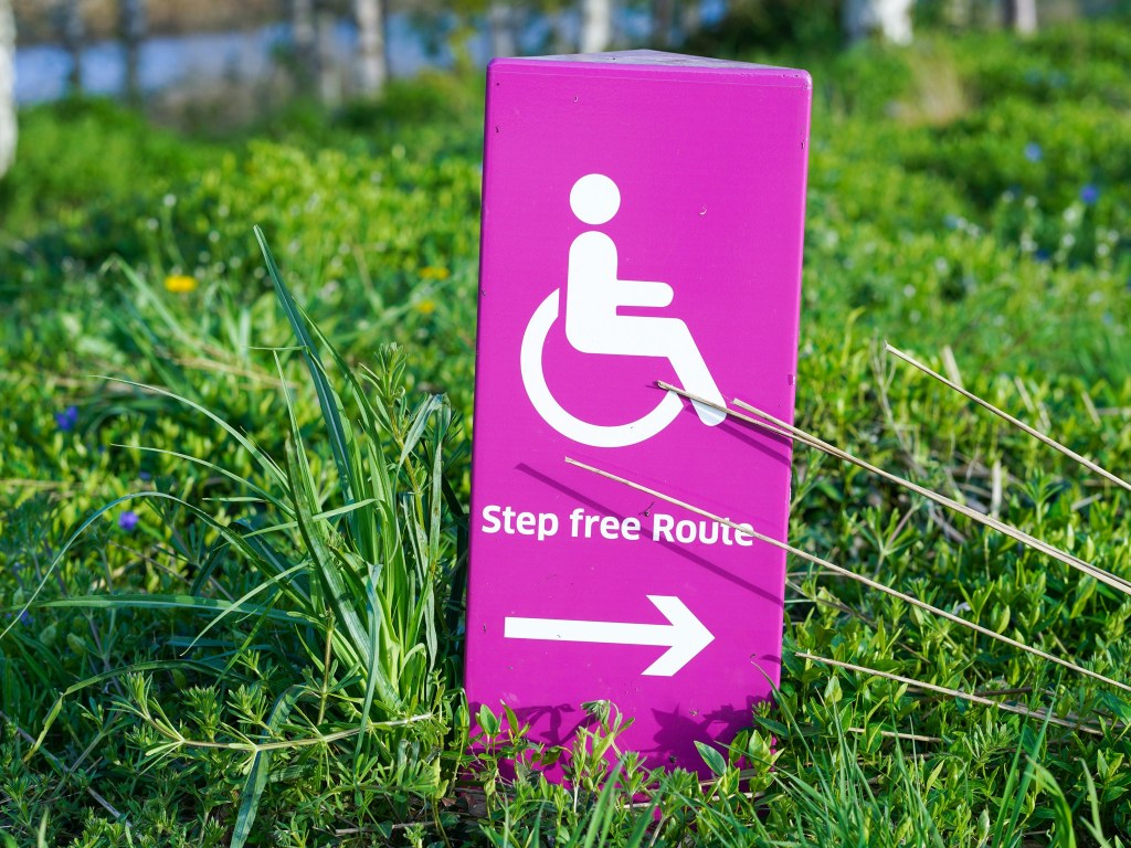 A pink accessible sign reading "Step free Route" sits in green grass