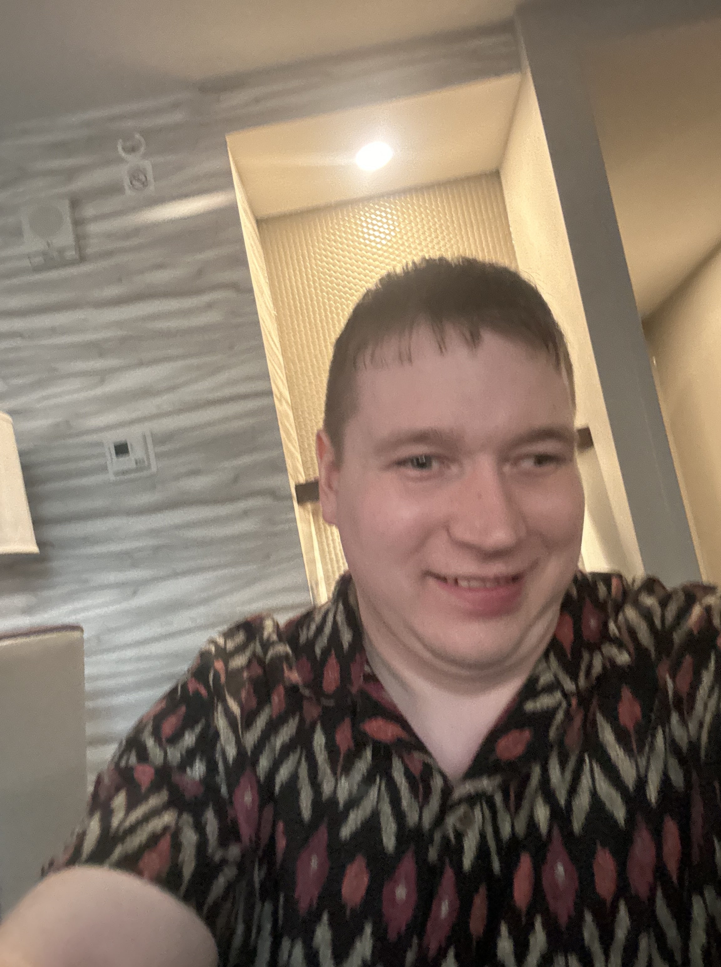 Justin smiles at the camera, he has short, brown hair, light-toned skin, and wears a geometric patterned shirt.