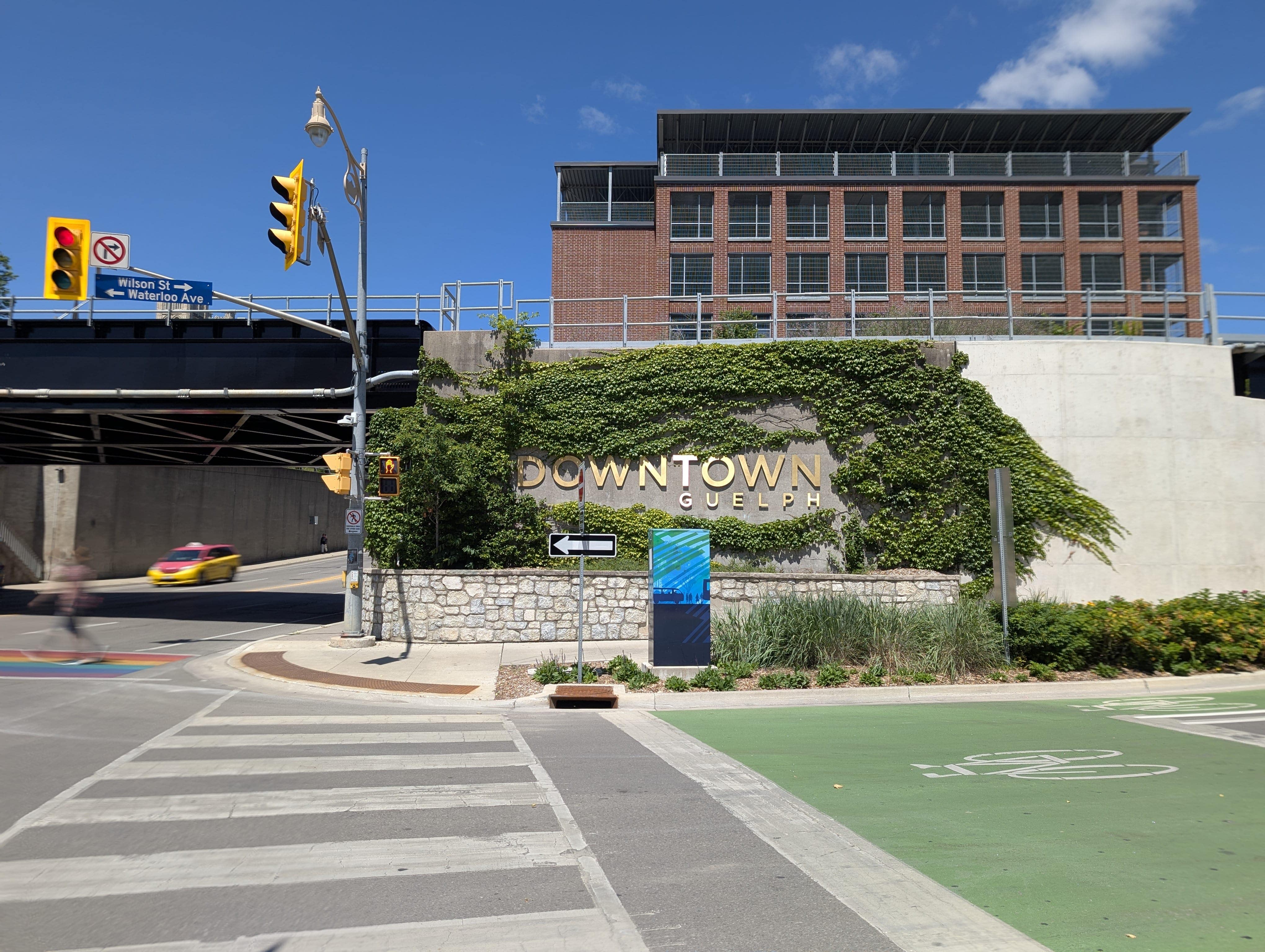 A busy intersection leading to Downtown Guelph is marked with a sign on a wall covered in green plants.