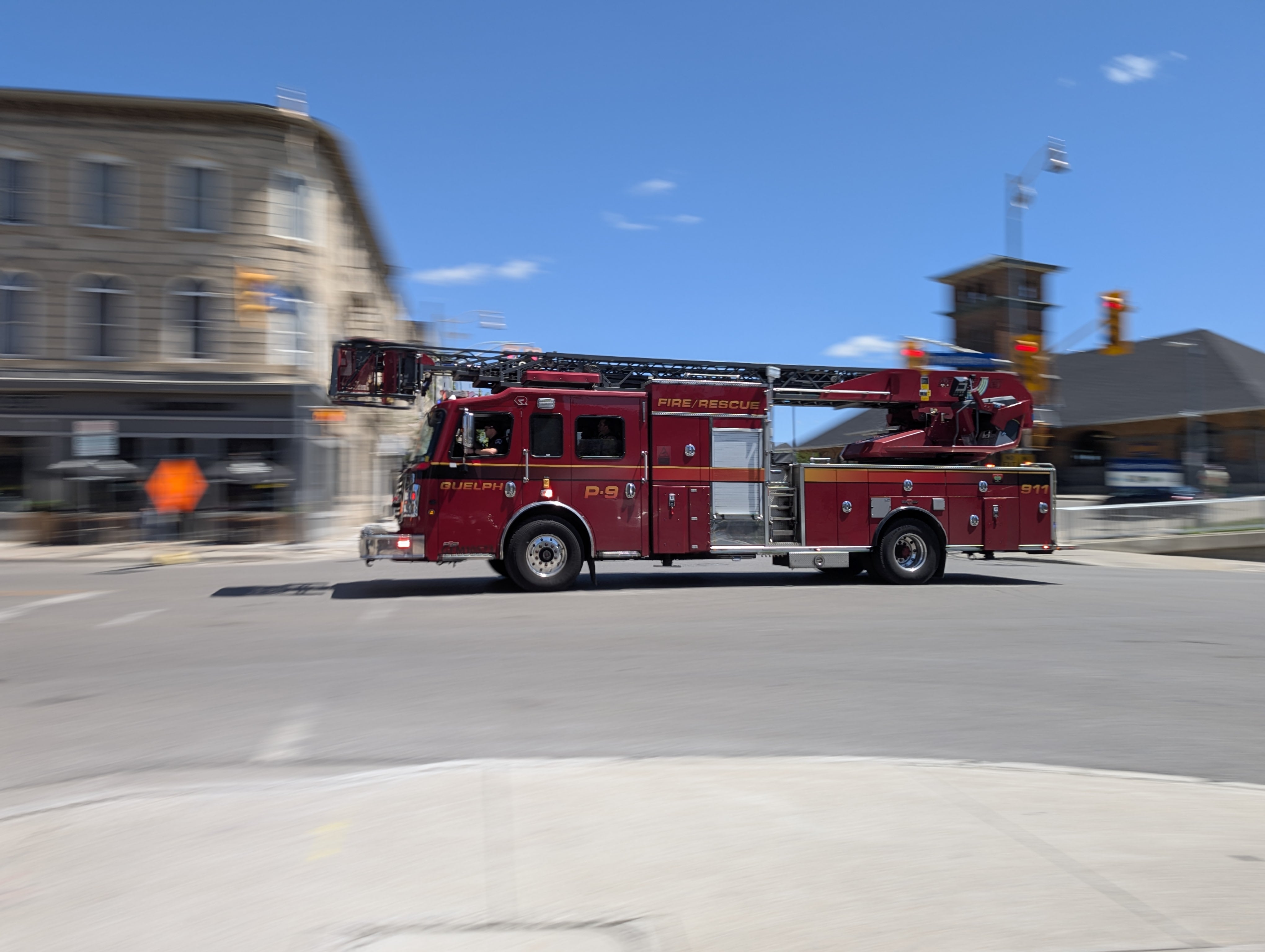 A red fire truck races through a downtown Guelph intersection in a dynamic shot.