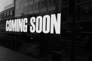 A black and white photo of the side of a building with large white letters that spell: "Coming Soon"